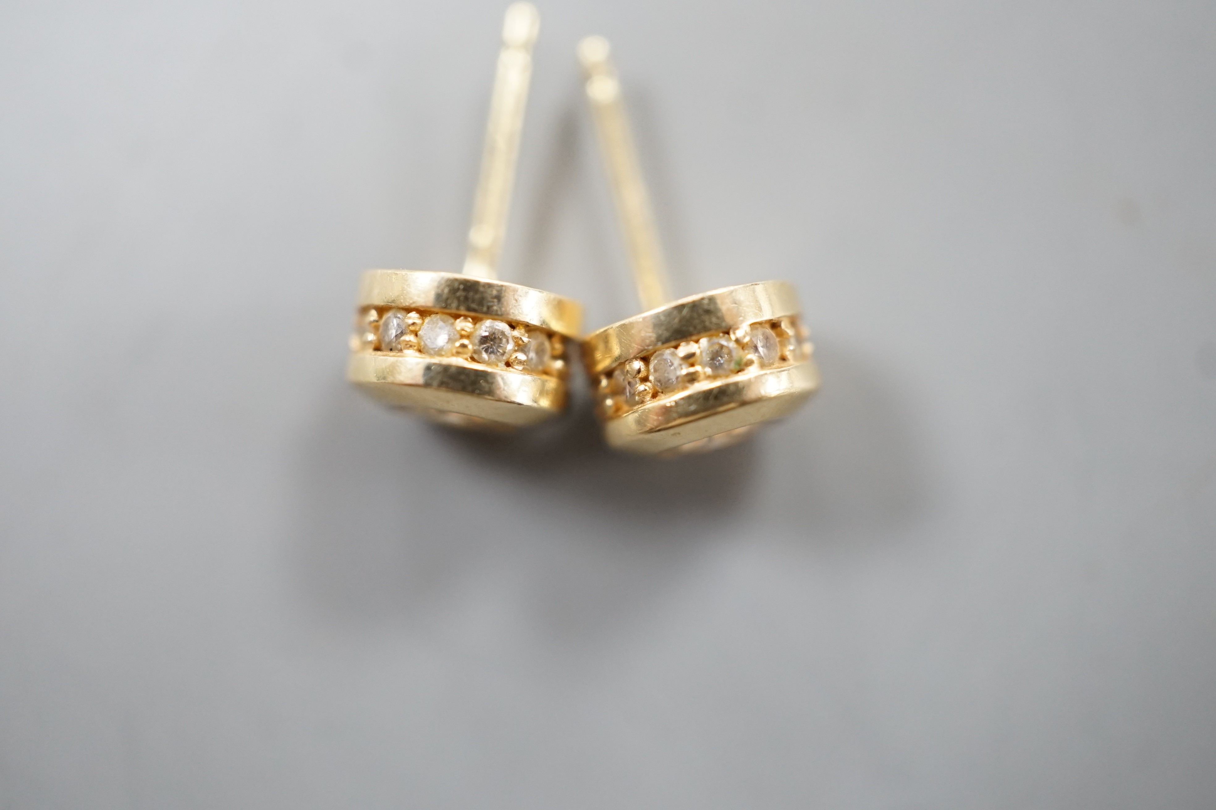 A modern pair of 14k yellow metal and single stone diamond set ear studs, with diamond chip setting, diameter 6mm, gross weight 2.8 grams.